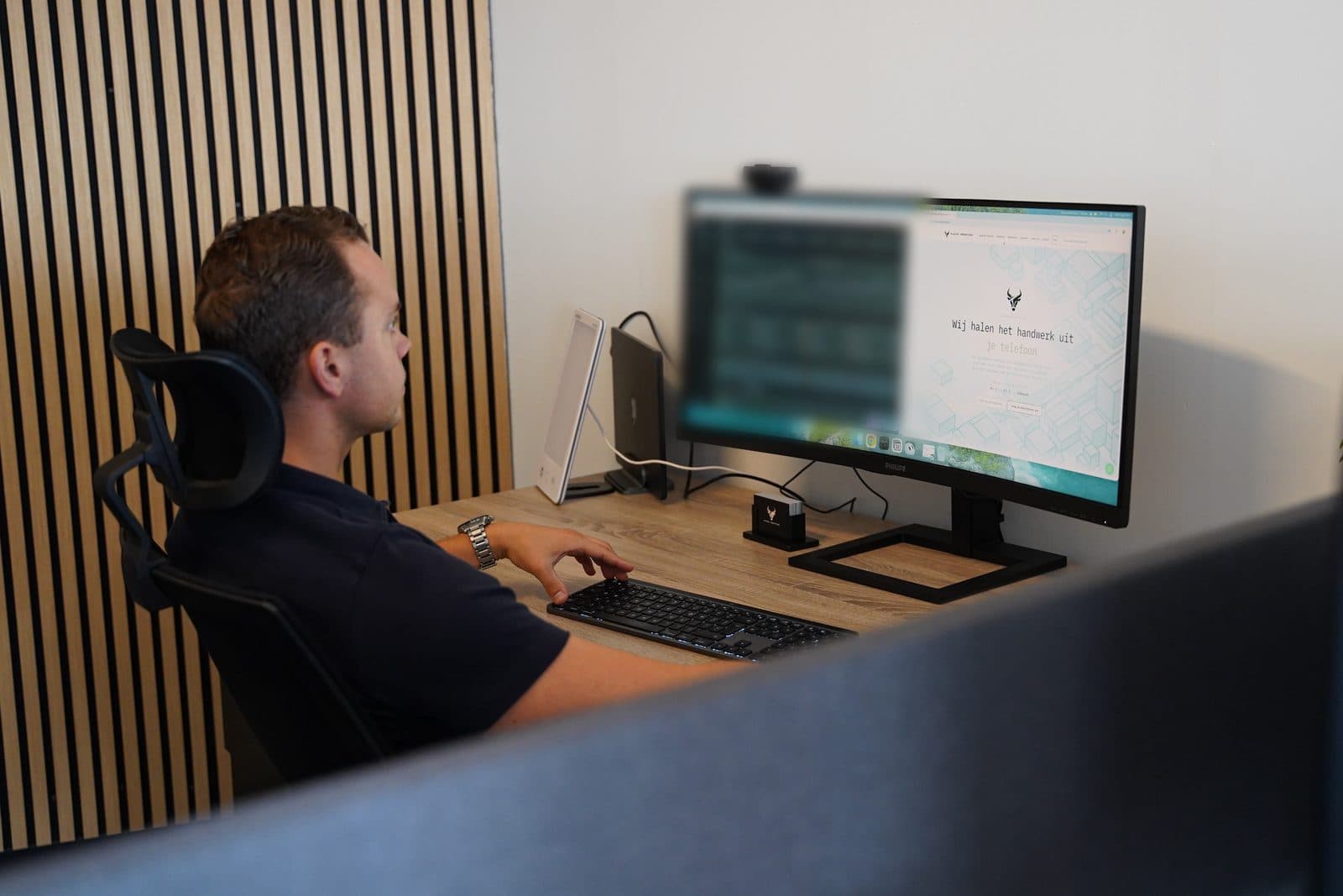 Een ontwikkelaar aan een bureau op het kantoor van Elusive kijkt naar een breed scherm, de linkerhelft van het scherm onscherp gemaakt